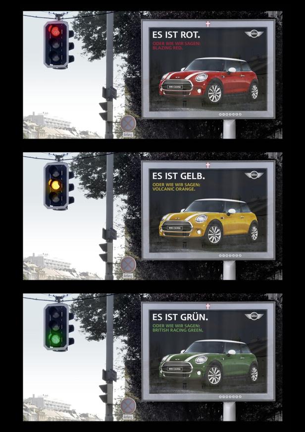Eine Ampel zeigt Rot, Gelb und Grün neben drei Werbetafeln für den Mini Cooper in den gleichen Farben.