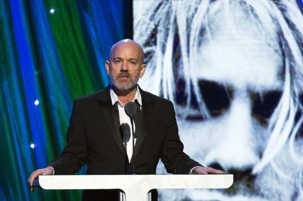 Michael Stipe bei einer Rede vor einem großen Porträt.