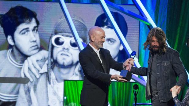 Dave Grohl nimmt eine Auszeichnung entgegen, im Hintergrund ein Bild von Nirvana.
