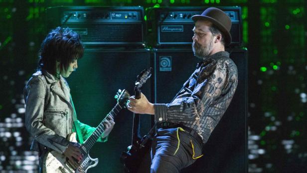 Zwei Gitarristen treten vor Verstärkern auf einer Bühne auf.