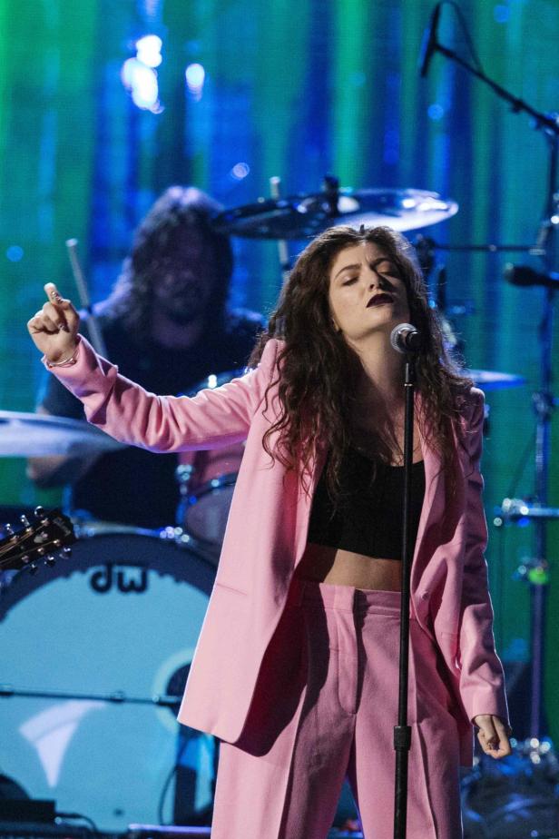 Lorde tritt in einem pinkfarbenen Hosenanzug auf einer Bühne auf.