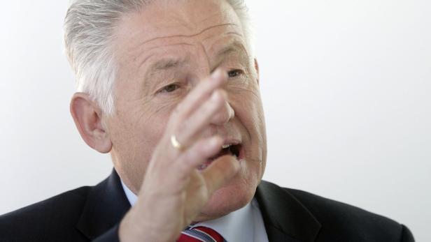 Ein älterer Mann mit Anzug gestikuliert und spricht.