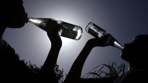 Zwei Personen trinken aus Glasflaschen vor einem hellen Himmel.