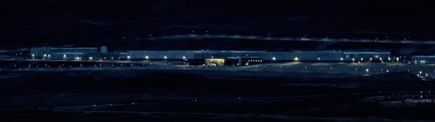 Eine nächtliche Aufnahme eines großen, beleuchteten Gebäudekomplexes in einer hügeligen Landschaft.
