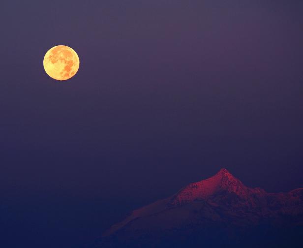 Ein Vollmond über einem Bergmassiv in der Abenddämmerung.