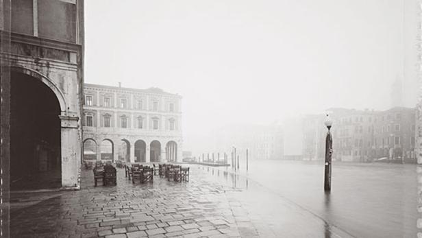 Ein Platz in Venedig mit Tischen und Stühlen am Wasser in dichtem Nebel.