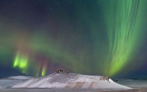 Eine Gruppe von Menschen beobachtet die Nordlichter über einer verschneiten Landschaft.