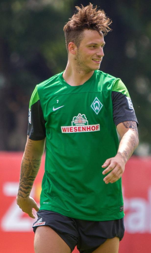 Ein junger Mann im grünen Trikot von Werder Bremen mit Tattoos auf den Armen.