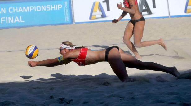 Eine Beachvolleyballspielerin hechtet nach dem Ball im Sand.