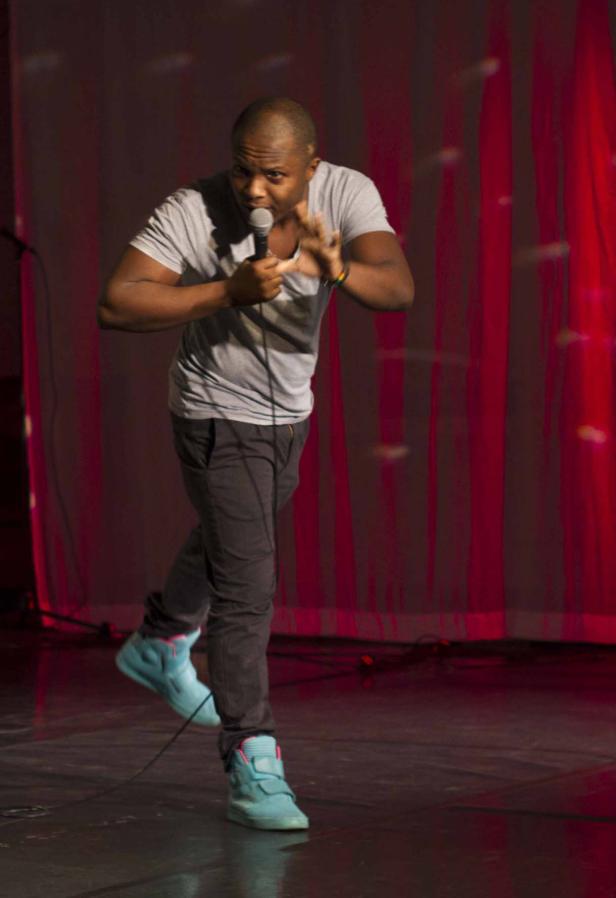 Ein Mann mit Mikrofon steht auf einer Bühne vor einem roten Vorhang.