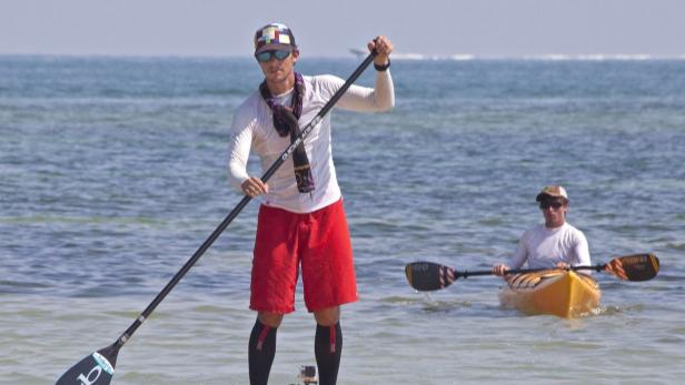 Ein Mann steht auf einem Paddleboard und ein anderer fährt Kajak im Meer.