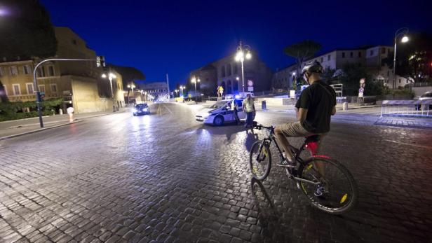 Ein Radfahrer steht nachts auf einer Kopfsteinpflasterstraße in der Nähe eines Polizeiautos.