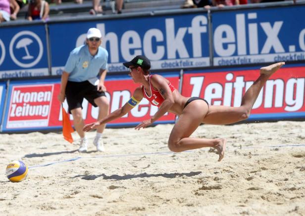 Eine Beachvolleyballspielerin hechtet nach dem Ball, während ein Schiedsrichter zusieht.