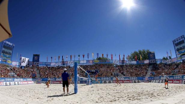 Ein Beachvolleyballspiel vor einer großen Zuschauermenge unter blauem Himmel.