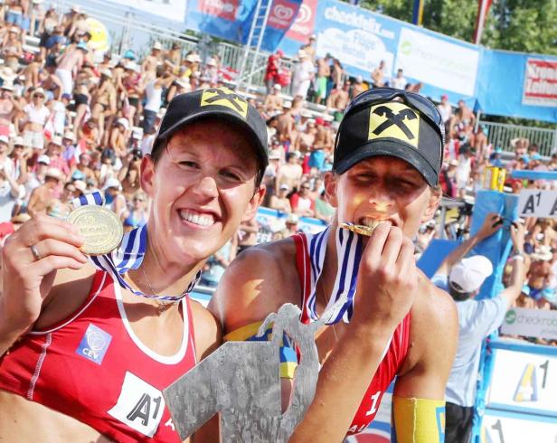 Zwei Beachvolleyballspielerinnen feiern ihren Sieg mit Medaillen und einer Trophäe.