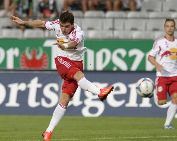 Ein Fußballspieler in rot-weißem Trikot schießt einen Ball.