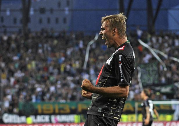 Ein Fußballspieler jubelt mit geballten Fäusten vor einer Zuschauermenge.