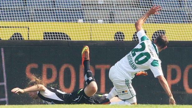 Ein Fußballspieler stürzt, während ein anderer mit der Nummer 20 daneben steht.