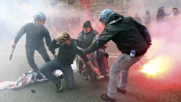 Bei einer Demonstration greifen Personen in Schutzkleidung einen Mann im Rollstuhl an.