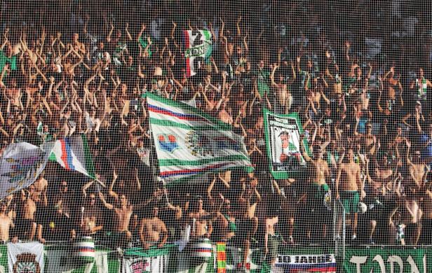 Eine große Menschenmenge, vermutlich Fußballfans, jubelt hinter einem Netz.
