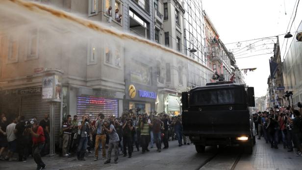 Ein Wasserwerfer sprüht Wasser in eine Menschenmenge in einer städtischen Straße.
