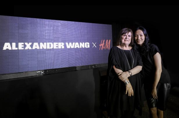 Zwei Frauen posieren vor einer Wand mit der Aufschrift „Alexander Wang x H&M“.