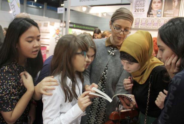 Eine Gruppe von Mädchen und eine Frau betrachten gemeinsam ein Buch.