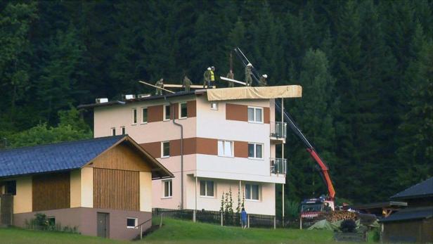 Arbeiter reparieren mit einem Kran das Dach eines mehrstöckigen Hauses.