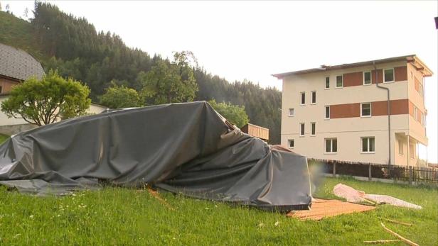 Ein mit einer Plane abgedeckter Gegenstand steht auf einer Wiese vor einem Gebäude.