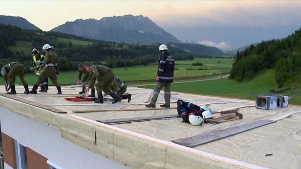 Eine Gruppe von Feuerwehrleuten arbeitet auf einem Dach vor einer Bergkulisse.
