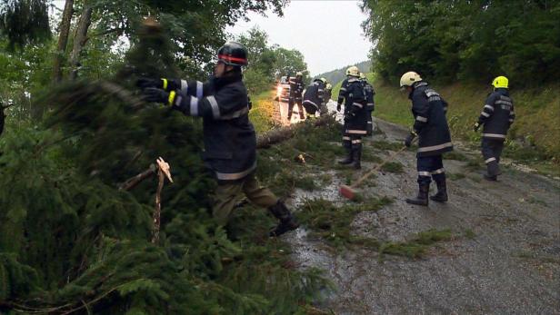 Feuerwehrleute räumen nach einem Sturm eine Straße von umgestürzten Bäumen frei.