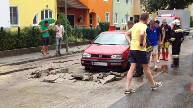 Ein rotes Auto steht vor einem durch einen Rohrbruch beschädigten Straßenabschnitt.