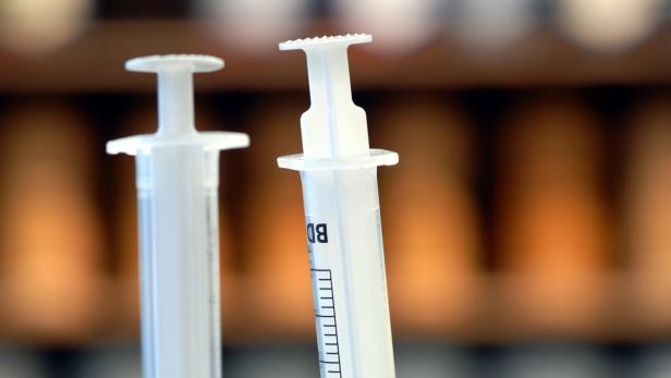 Zwei Spritzen stehen vor einem unscharfen, braunen Hintergrund.