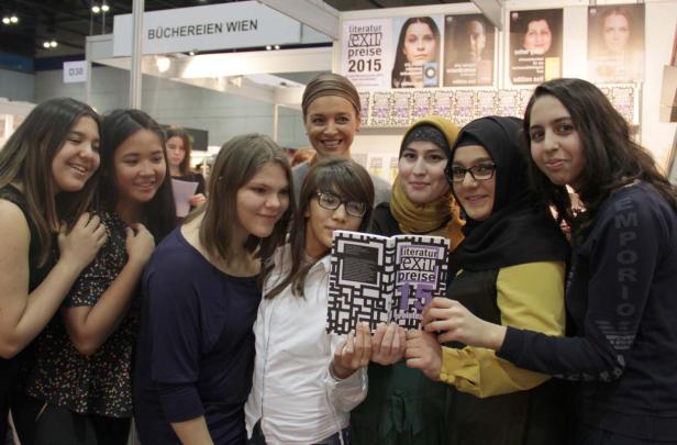 Eine Gruppe junger Frauen posiert mit dem Buch „Literaturpreise Exit 15“ auf einer Buchmesse.