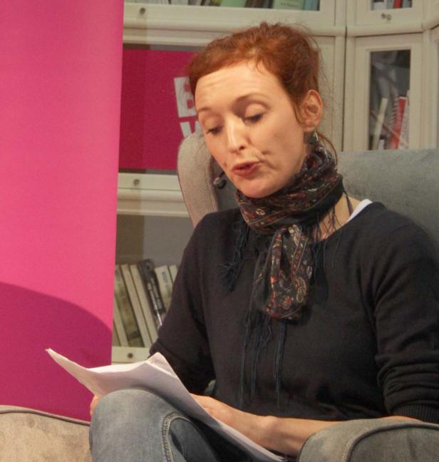 Eine Frau mit roten Haaren sitzt in einem Sessel und liest ein Dokument.