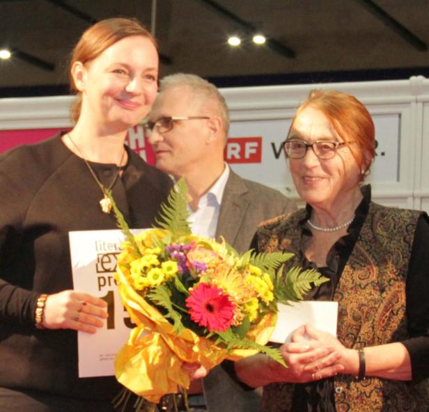 Zwei Frauen und ein Mann stehen mit einem Blumenstrauß auf einer Bühne.