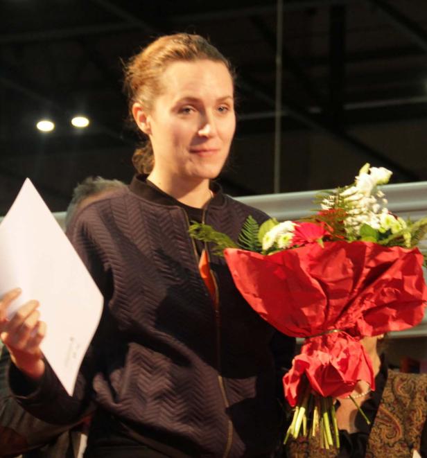 Eine Frau hält ein Dokument und einen Blumenstrauß.