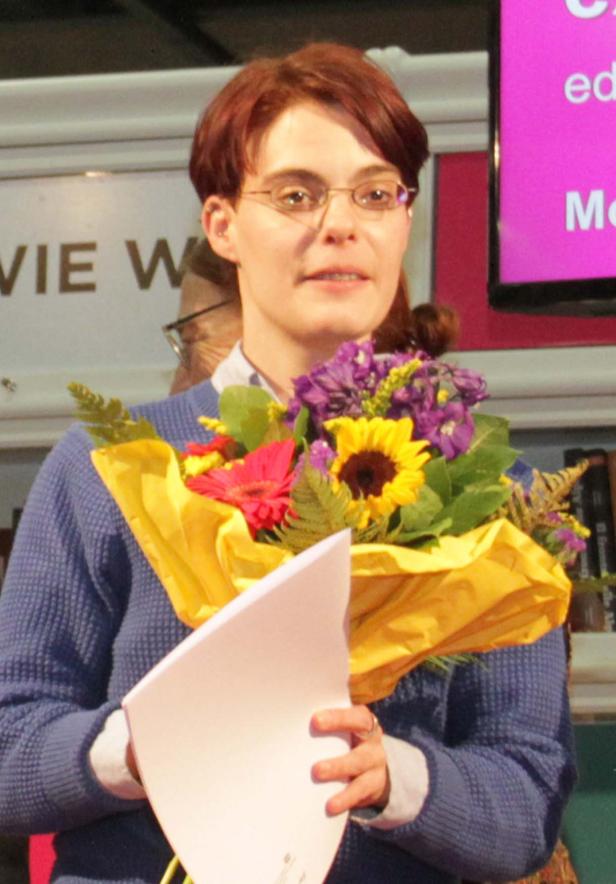 Eine Frau mit Brille hält einen Blumenstrauß und ein Dokument.