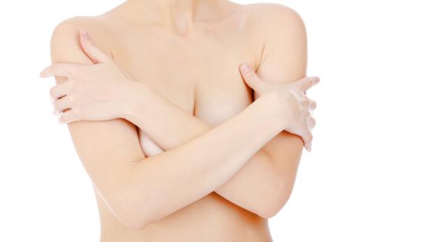 Eine Frau umarmt sich selbst vor einem weißen Hintergrund.