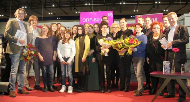 Eine Gruppe von Menschen steht auf einer Bühne mit Blumensträußen und Büchern.