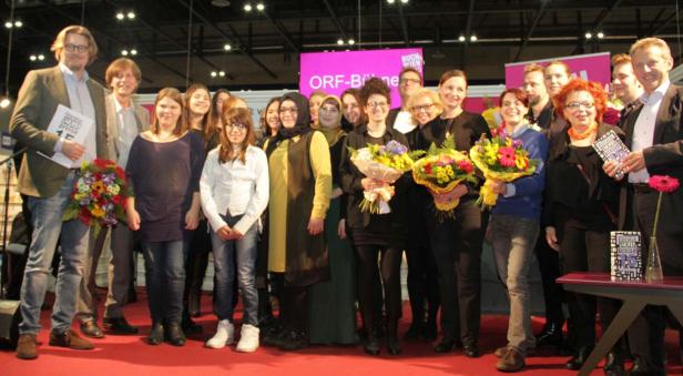 Eine Gruppe von Menschen steht auf einer Bühne mit Blumensträußen.