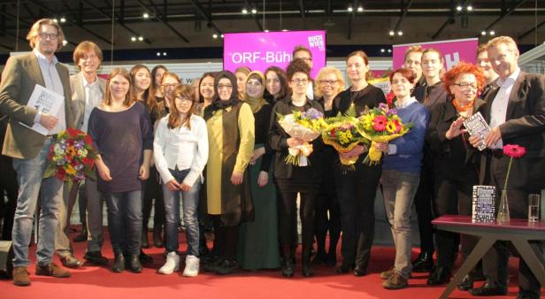 Eine Gruppe von Menschen posiert auf einer Bühne mit Blumensträußen und Büchern.