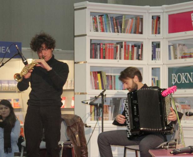 Zwei Musiker spielen Saxophon und Akkordeon vor einem Bücherregal.