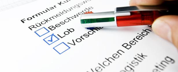 Ein Formular mit einem angekreuzten Kästchen für „Lob“ wird mit einem Stift ausgefüllt.