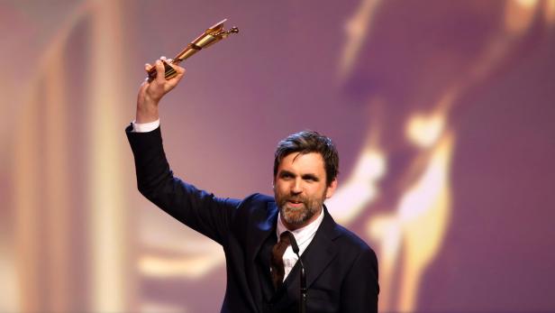 Beim Deutschen Filmpreis als Bester Regisseur ausgezeichnet: Sebastian Schipper Ein Mann im Anzug hält eine goldene Trophäe in die Höhe.