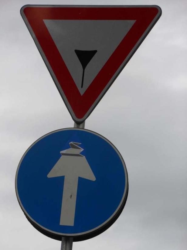 Ein „Vorfahrt gewähren!“-Schild über einem Schild, das eine obligatorische Fahrtrichtung geradeaus anzeigt.