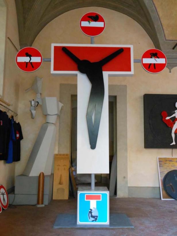 Eine Kreuz-Skulptur aus Verkehrsschildern in einem Innenraum.