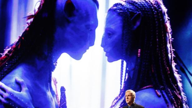 James Cameron vor einer Szene mit zwei Na'vi aus dem Film „Avatar: The Way of Water“.