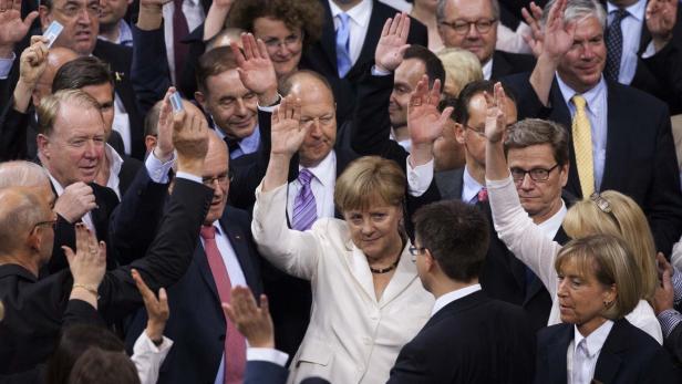 Angela Merkel und andere Politiker stimmen mit erhobenen Händen ab.
