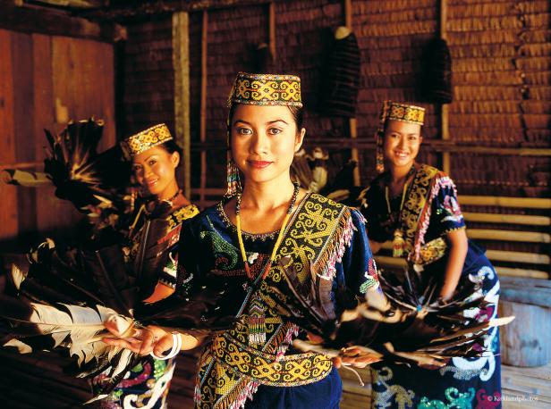 Drei Frauen in traditioneller Kleidung mit Federfächern in einem Haus.